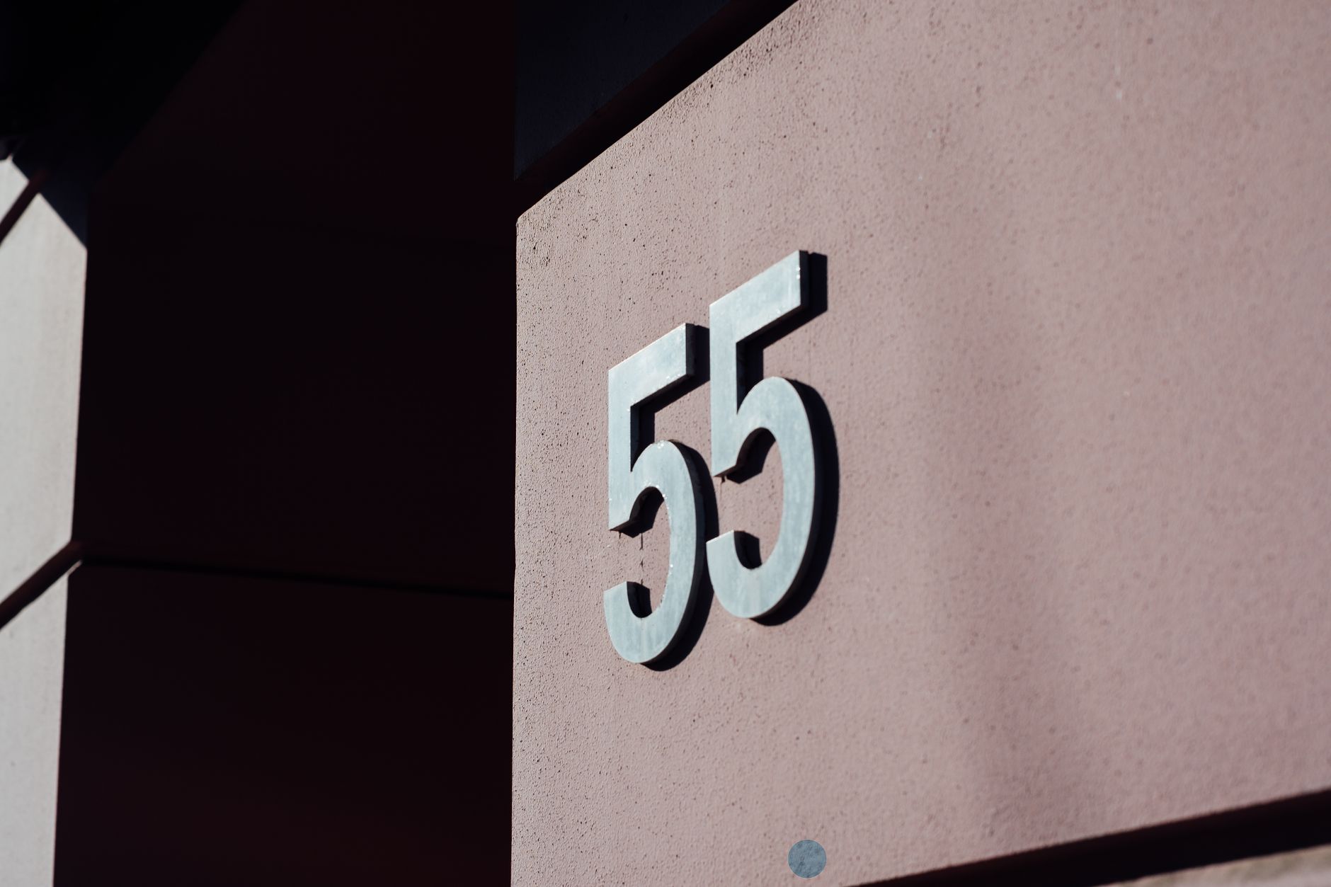 Close-up of a modern building wall with metal number 55 casting a shadow.