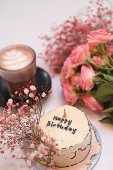 Elegant birthday setup featuring cake, coffee, and pink flowers.