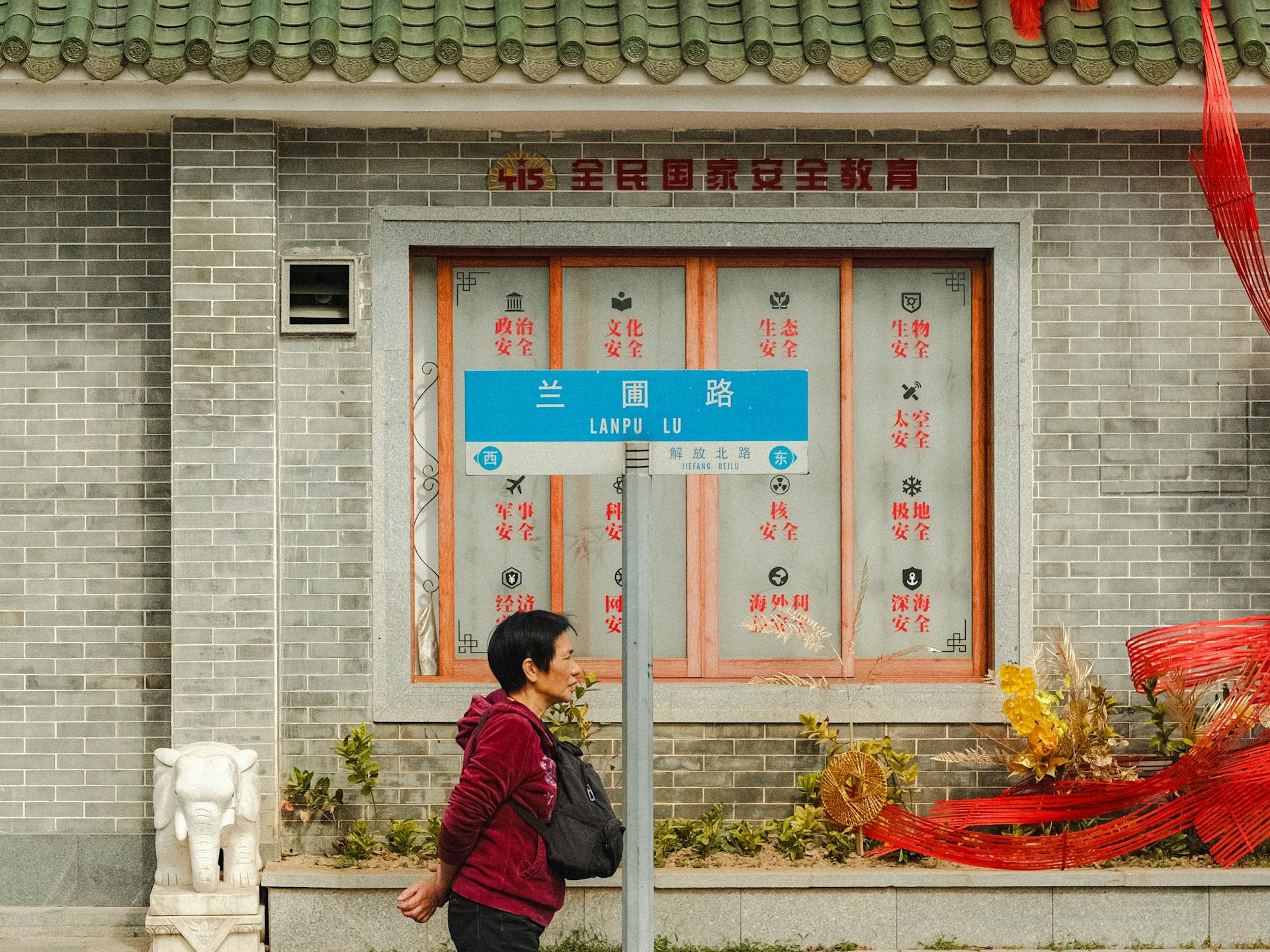 An outdoor urban scene featuring a person walking past an ornate building with a street sign in Chinese characters.