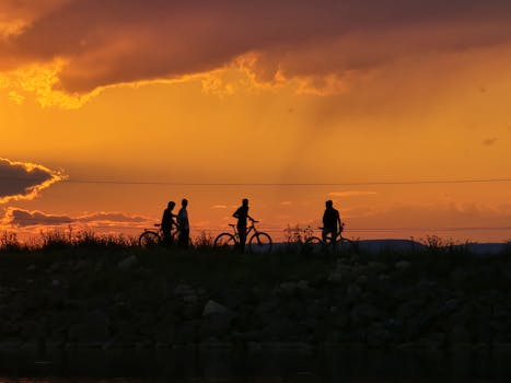 Silhouettes of cyclists during a stunning orange sunset over an open field.