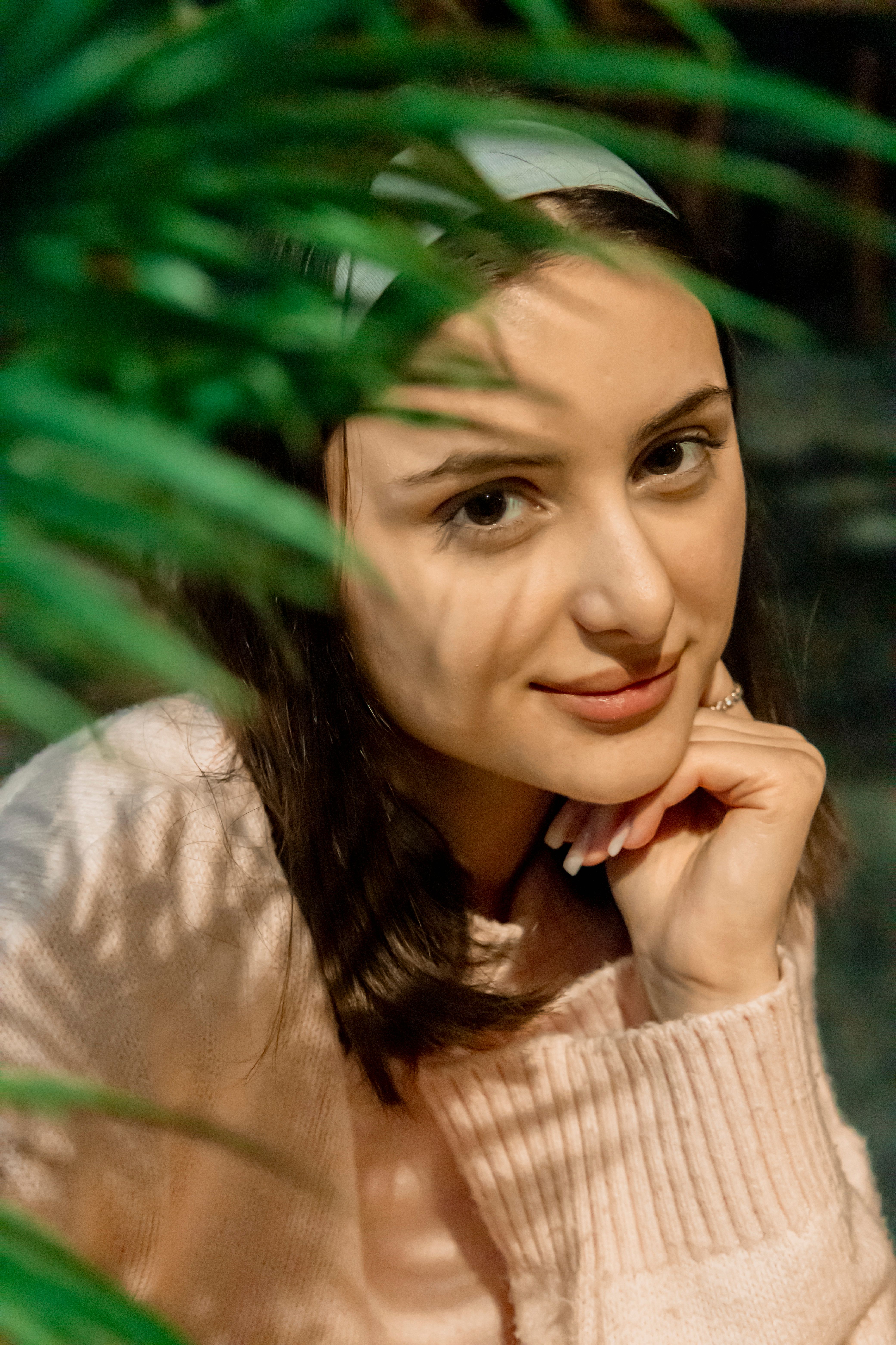 Gratuit O tânără într-un pulover confortabil zâmbește printre frunzele verzi luxuriante. Fotografie de stoc