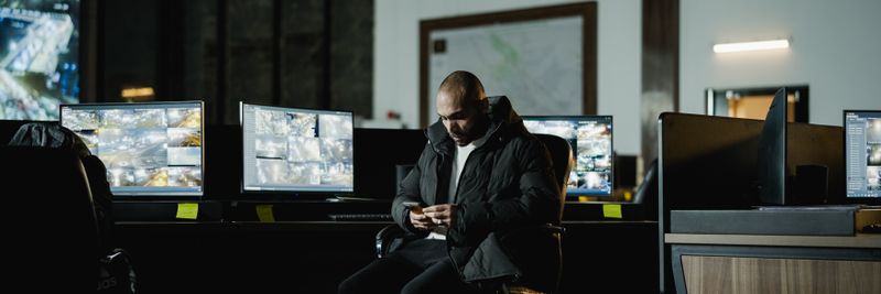 Security officer seated in a dimly lit control room, analyzing multiple surveillance screens.