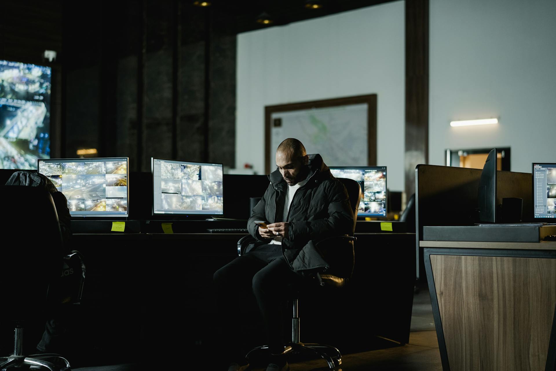 Security officer seated in a dimly lit control room, analyzing multiple surveillance screens.