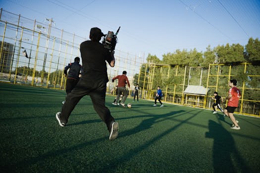 Cameraman captures an outdoor soccer game with players in action on a sunny day.