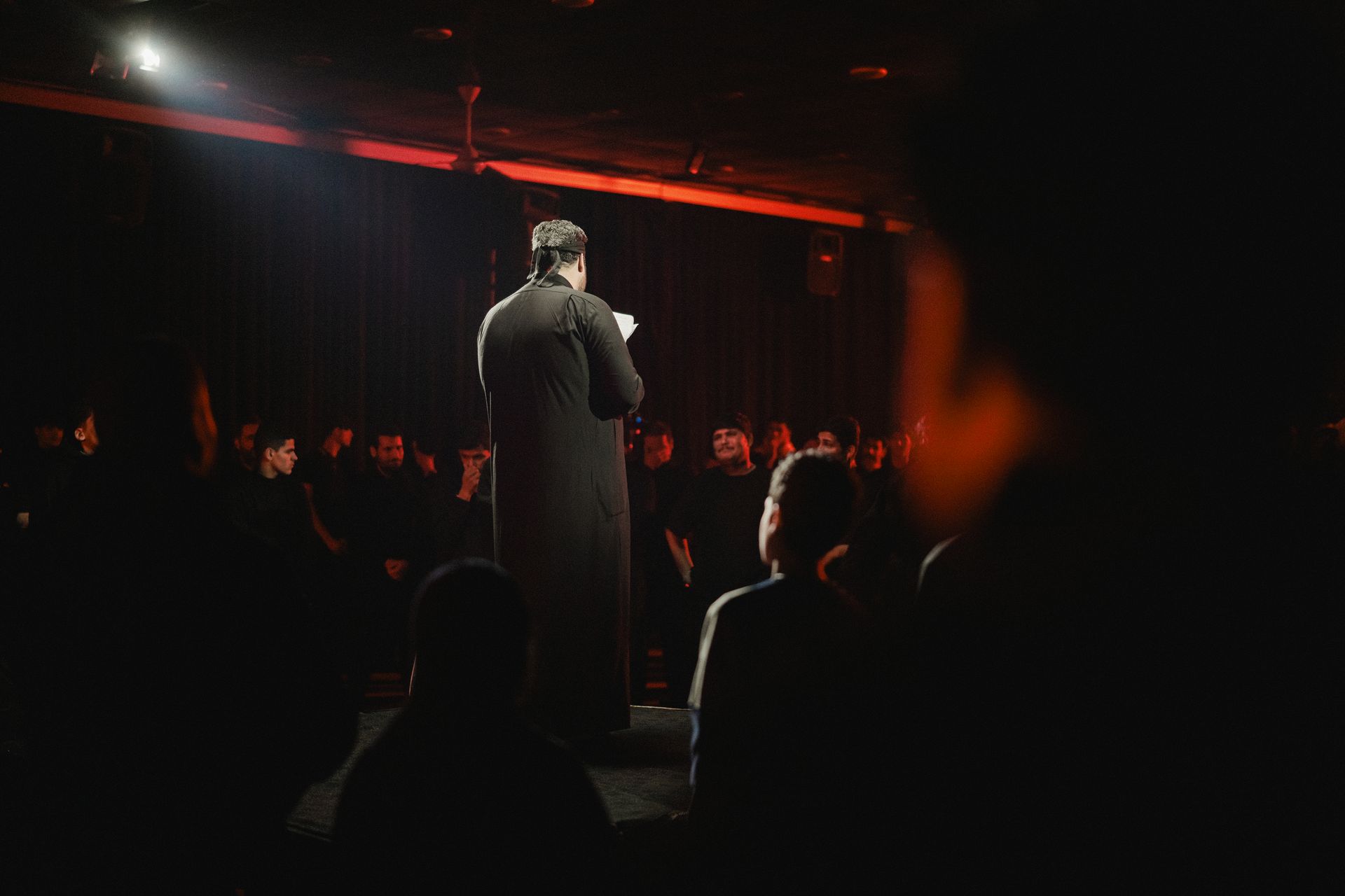 A speaker addresses an attentive audience in a dimly lit room, creating an intimate atmosphere.