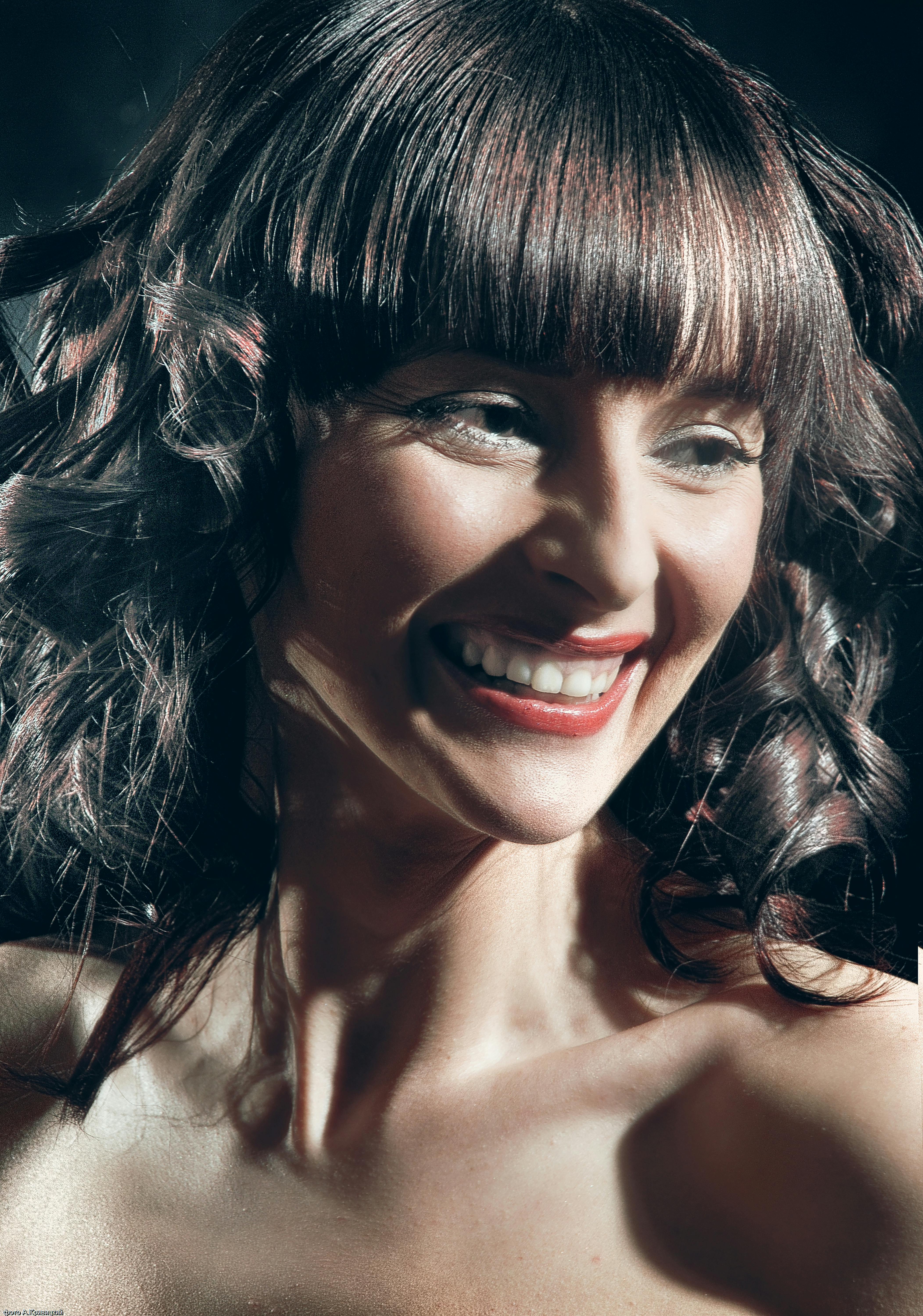 Portrait of a cheerful woman with curly hair and bangs, smiling brightly.