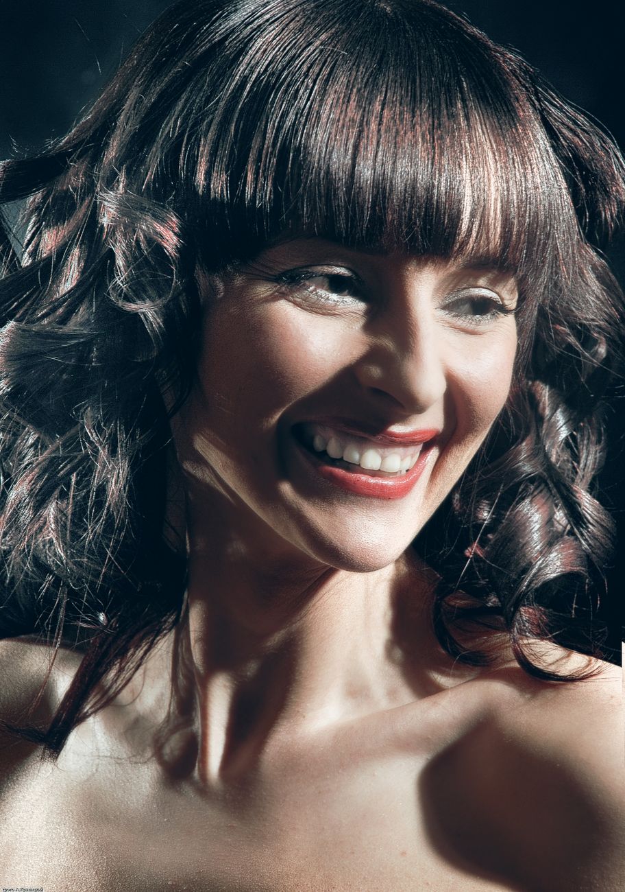 Portrait of a cheerful woman with curly hair and bangs, smiling brightly.