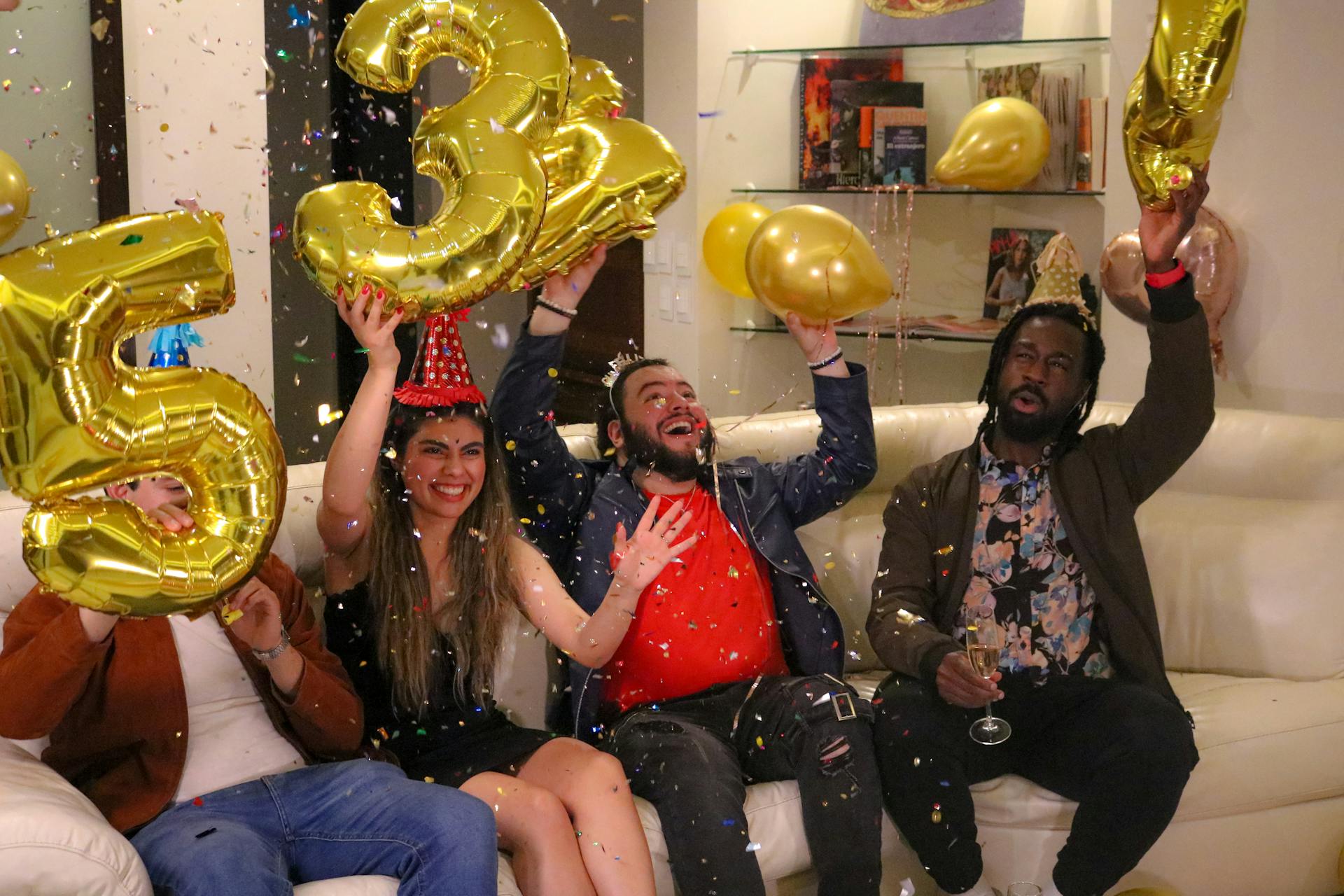 Joyful group celebrating with gold number balloons indoors.