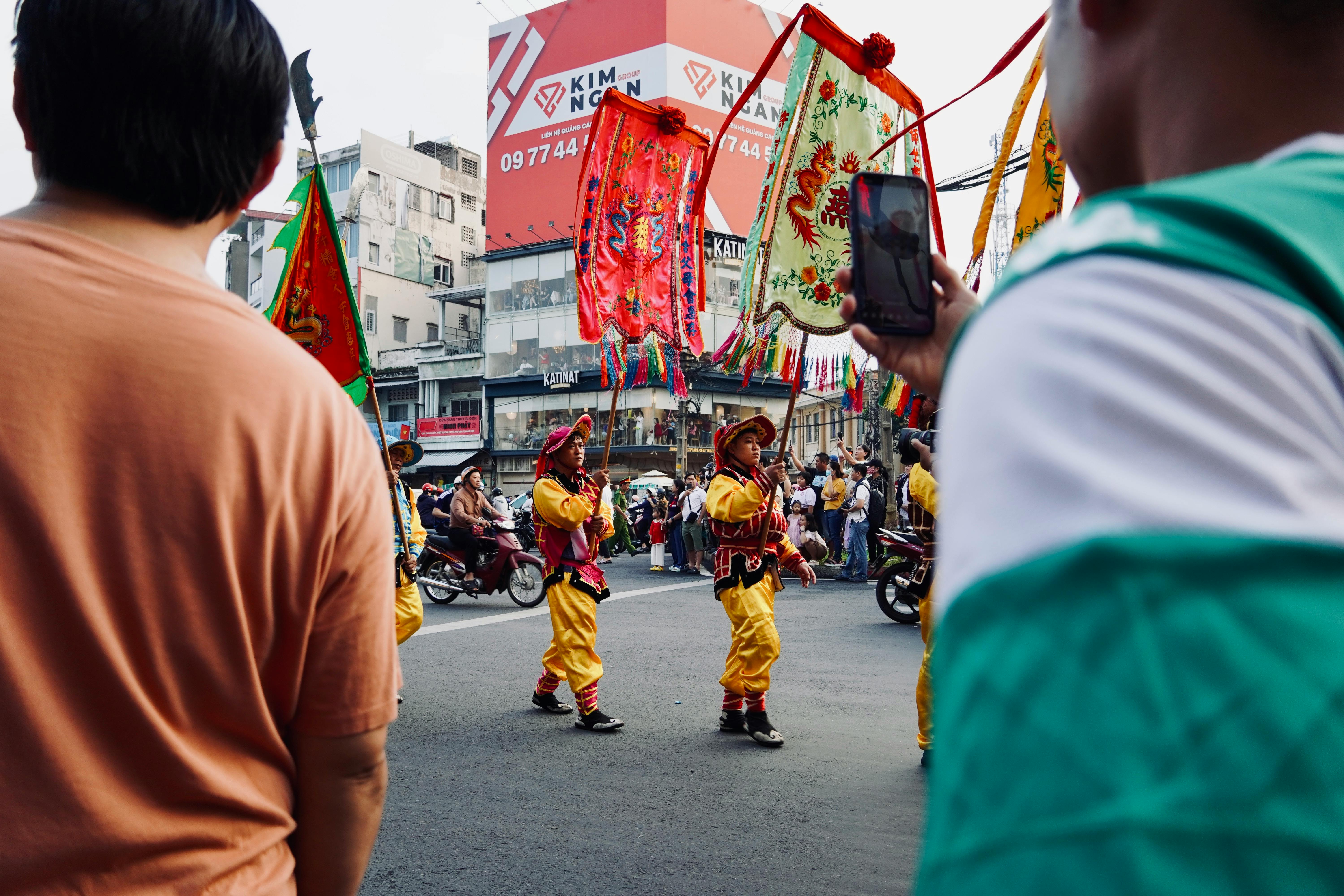 Vibrant street parade featuring performers in traditional attire holding colorful flags, crowded street.