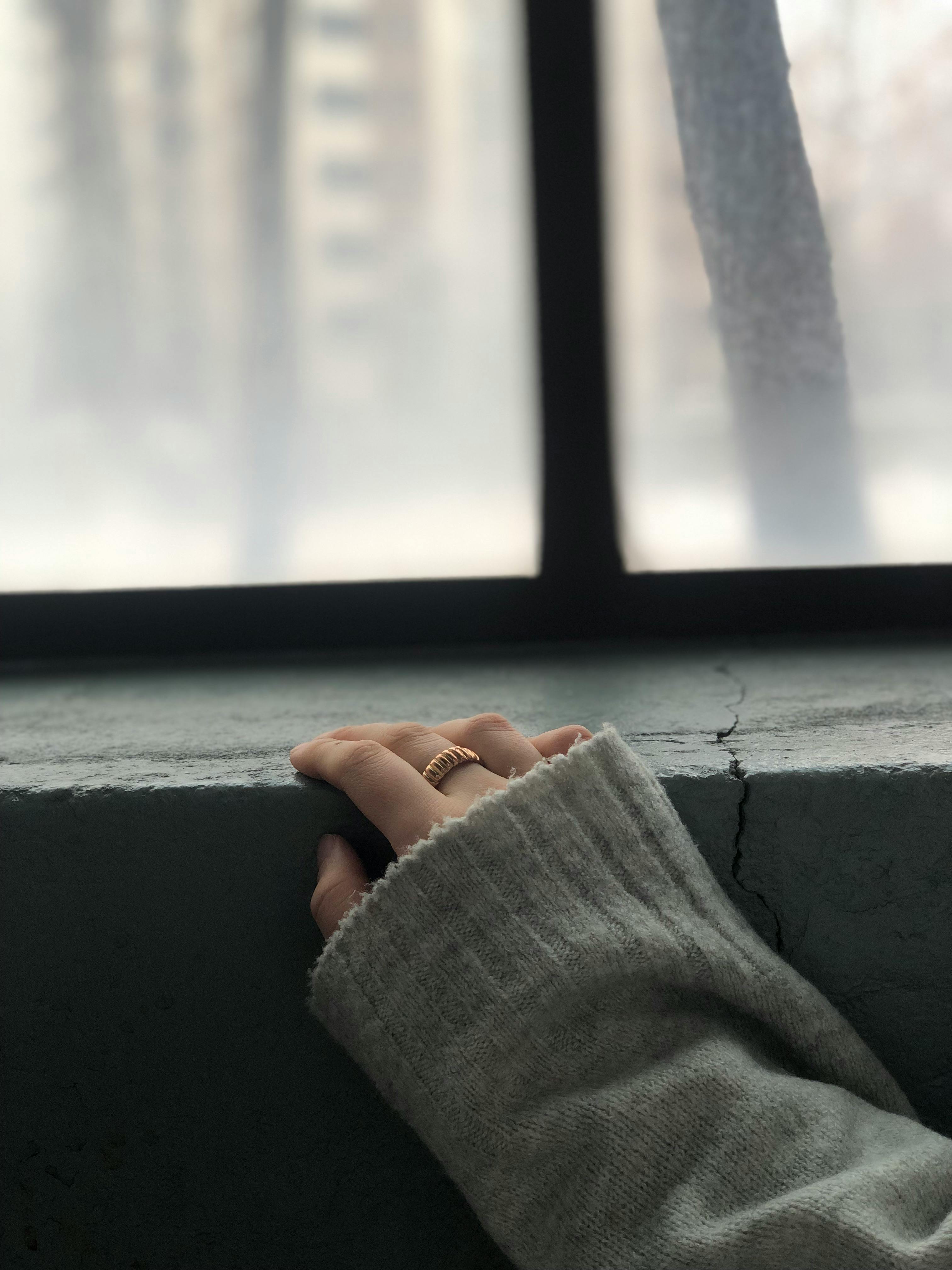 De franc Una mà que porta un anell daurat descansa sobre l'ampit d'una finestra amb un teló de fons d'hivern vaporós. Foto d'estoc