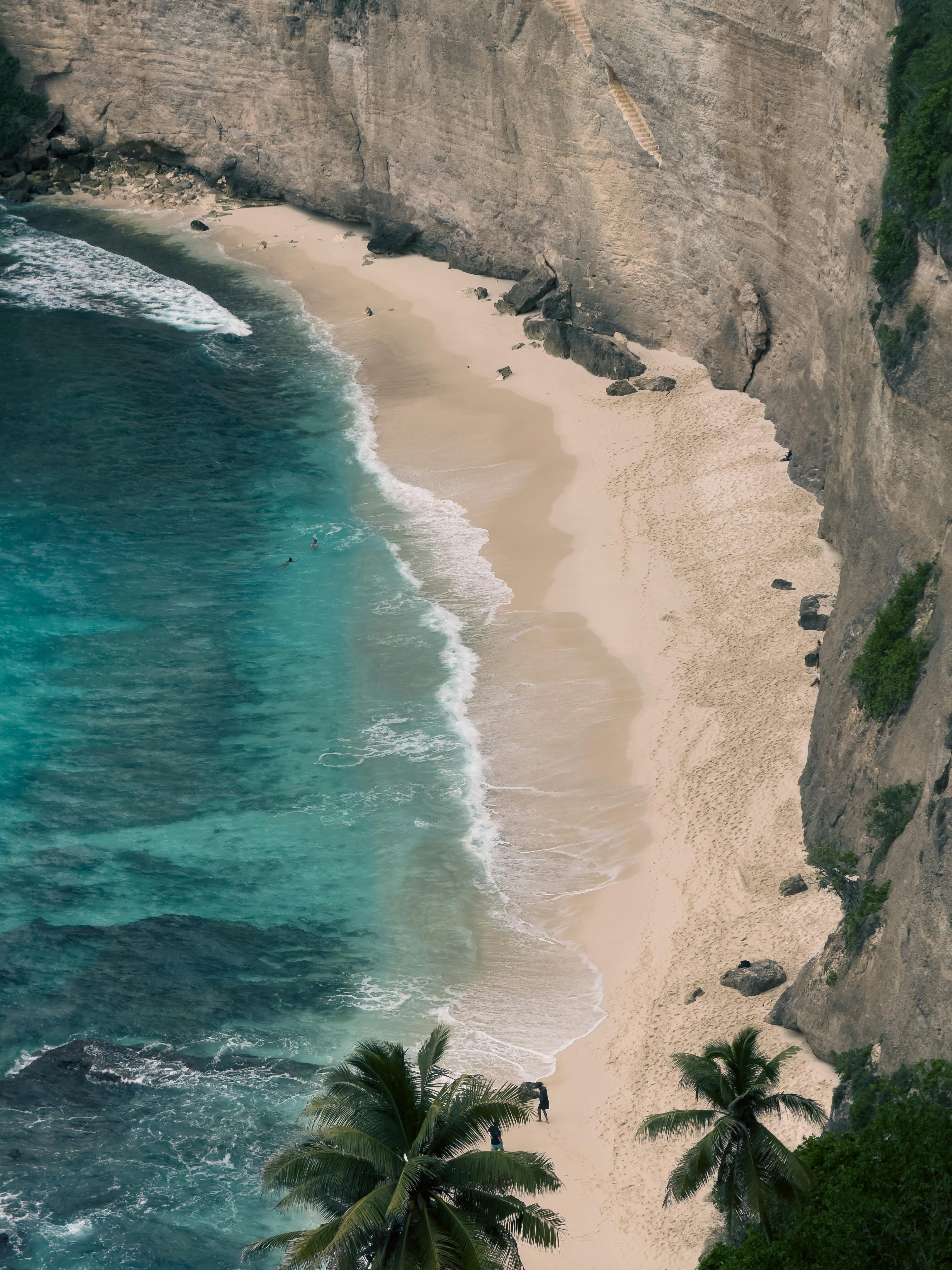 Aerial view of a secluded tropical beach with turquoise water and cliffside backdrop, Bali, Indonesia.