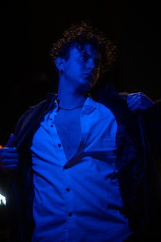 A dramatic urban portrait of a man under blue lighting, showcasing modern fashion and style.