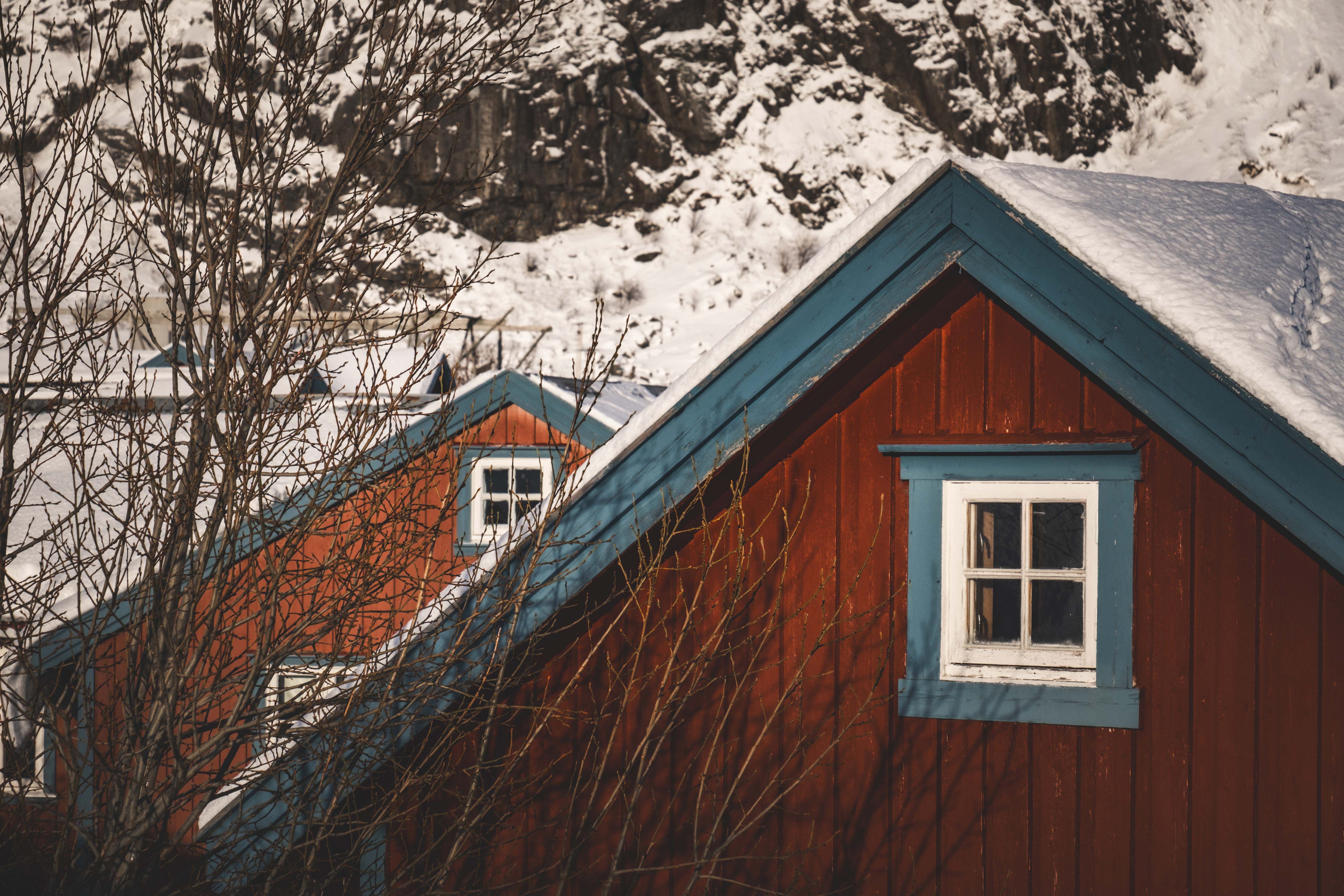 Cabane rouge recouverte de neige avec des garnitures bleues sur fond de montagnes accidentées.