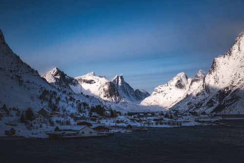 Free A picturesque snowy village nestled among the Lofoten mountains under a clear blue sky. Stock Photo