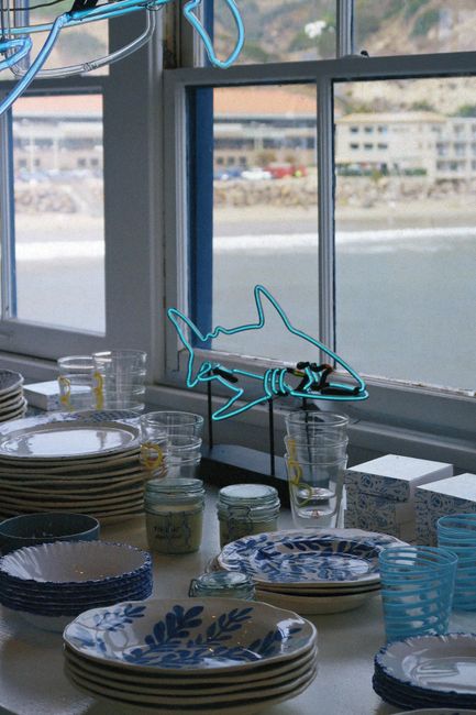 Blue and white tableware by window with neon shark overlooking the sea.