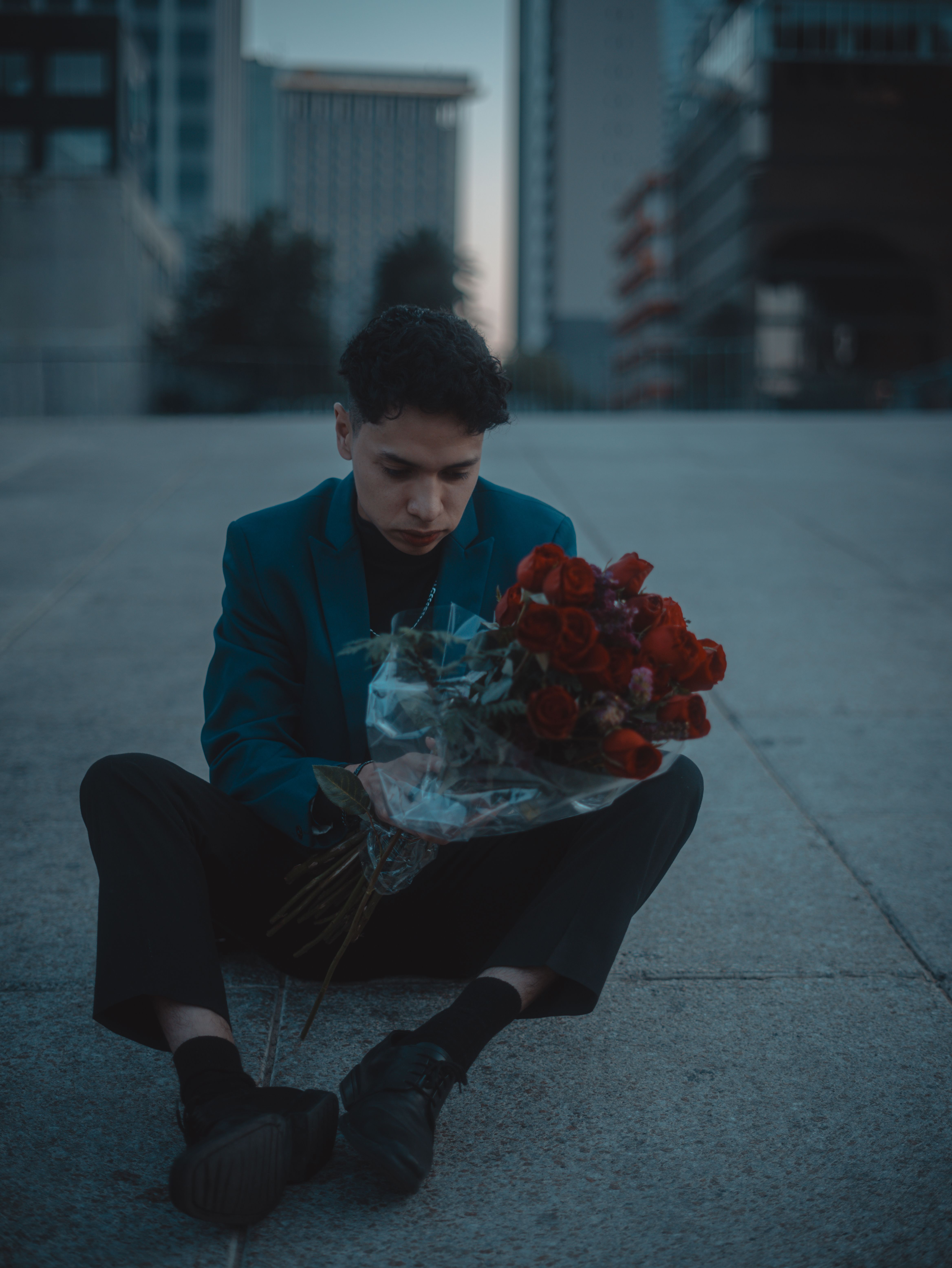 A man sits with a bouquet of roses in an urban setting, evoking a sense of romance and introspection.