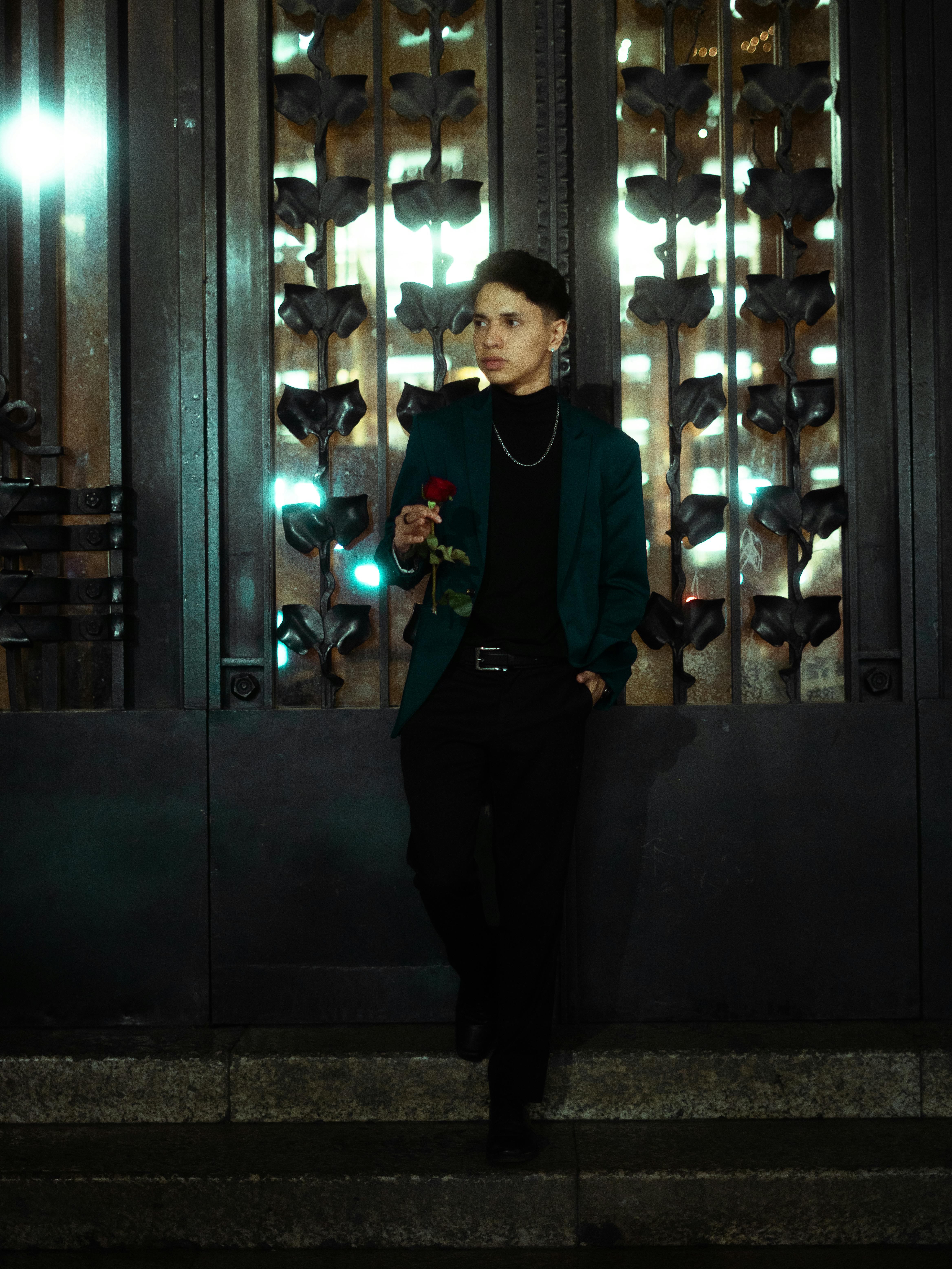 Portrait of a man holding a red rose in an urban setting at night, showcasing romantic and stylish themes.