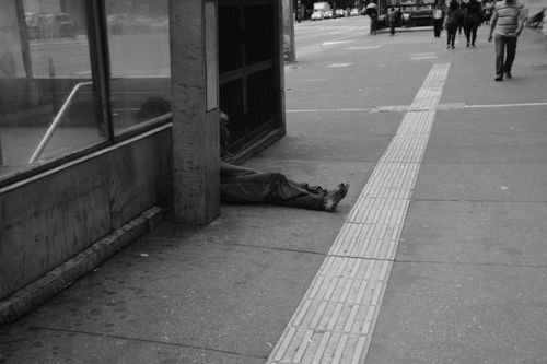 Free Black and white photo of a street scene with a person sitting in an urban area, highlighting urban life. Stock Photo