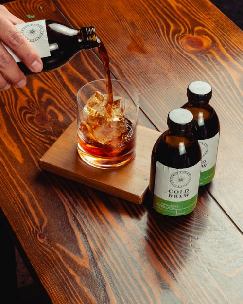 Free Close-up of cold brew coffee being poured over ice into a glass on a wooden table. Stock Photo