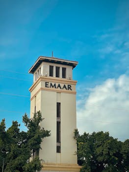 A scenic view of the Emaar tower against a bright blue sky with surrounding greenery.