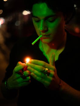 A man prepares to light a cigarette under green streetlight in Mexico City at night.