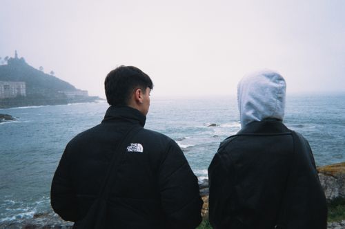 Free Two individuals overlooking a foggy ocean with rocky coastline, dressed warmly. Stock Photo