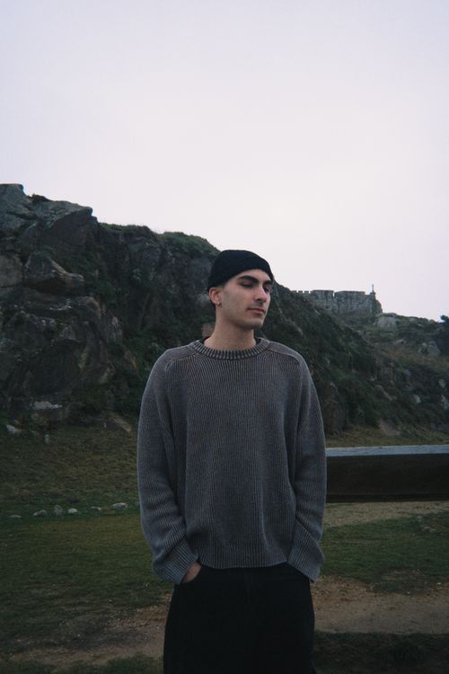 Free Young man in a sweater stands outdoors against a rocky landscape during daytime. Stock Photo
