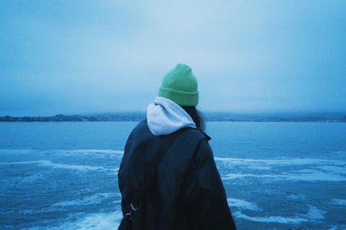 Free Person in green beanie and jacket gazing at a misty ocean on a winter day. Stock Photo