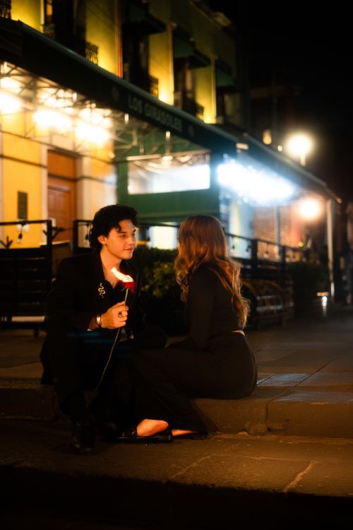 Free A couple shares a romantic moment sitting on a nighttime street in Mexico City, holding a rose. Stock Photo