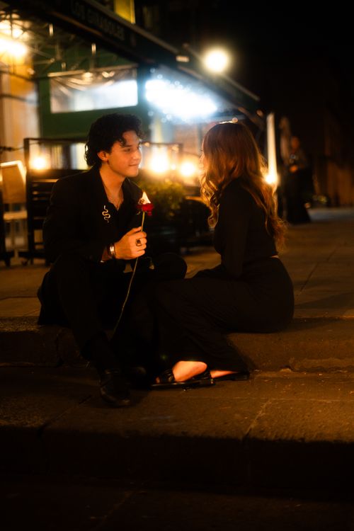 Free A couple enjoys a romantic evening outdoors with a red rose and warm lighting. Stock Photo