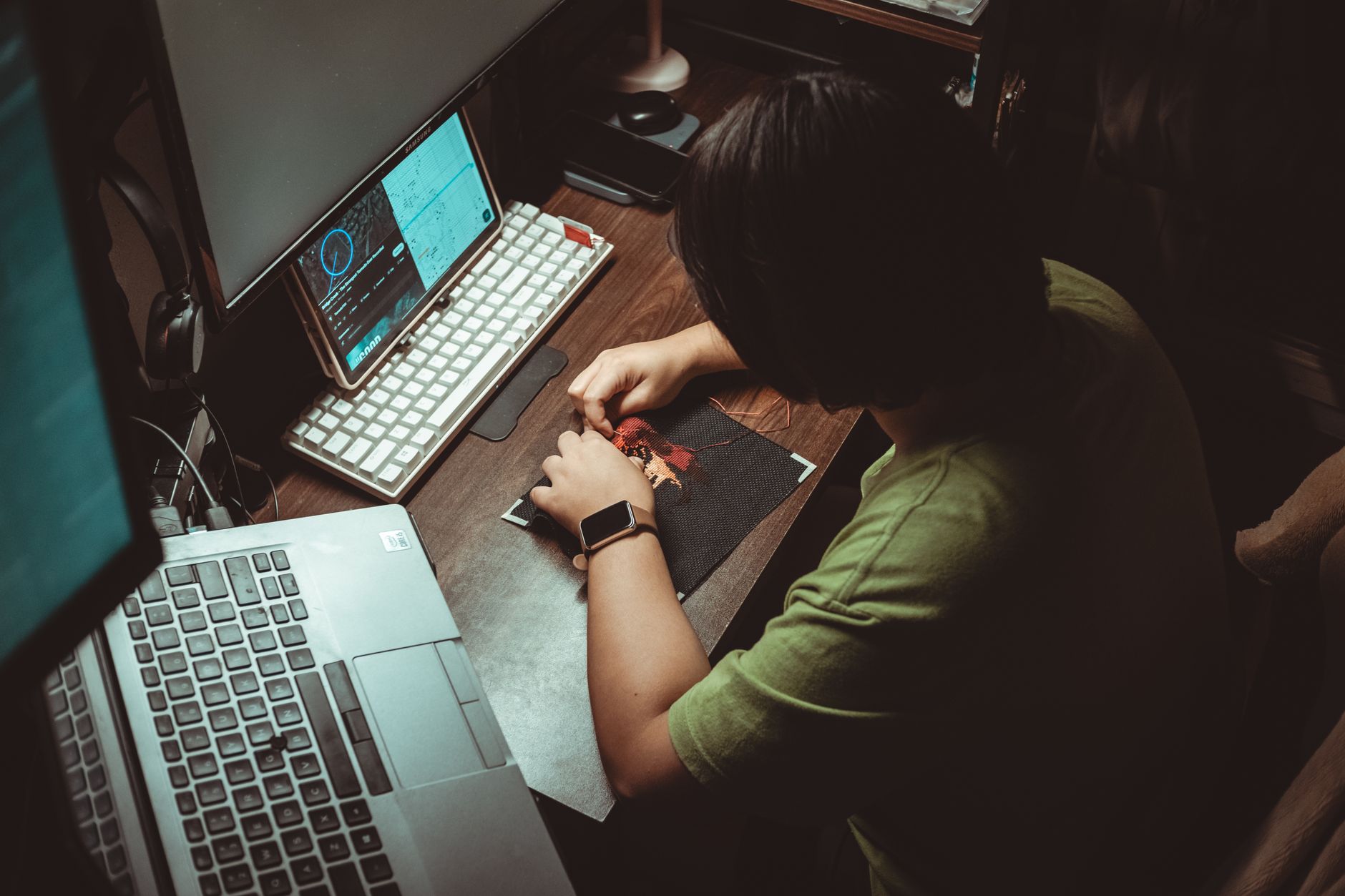 Person engaged in detailed artistic work at home office desk with technology tools.