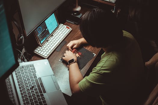 Person engaged in detailed artistic work at home office desk with technology tools.