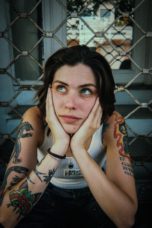 Free Portrait of a tattooed woman in thought, sitting outdoors against metal bars. Stock Photo