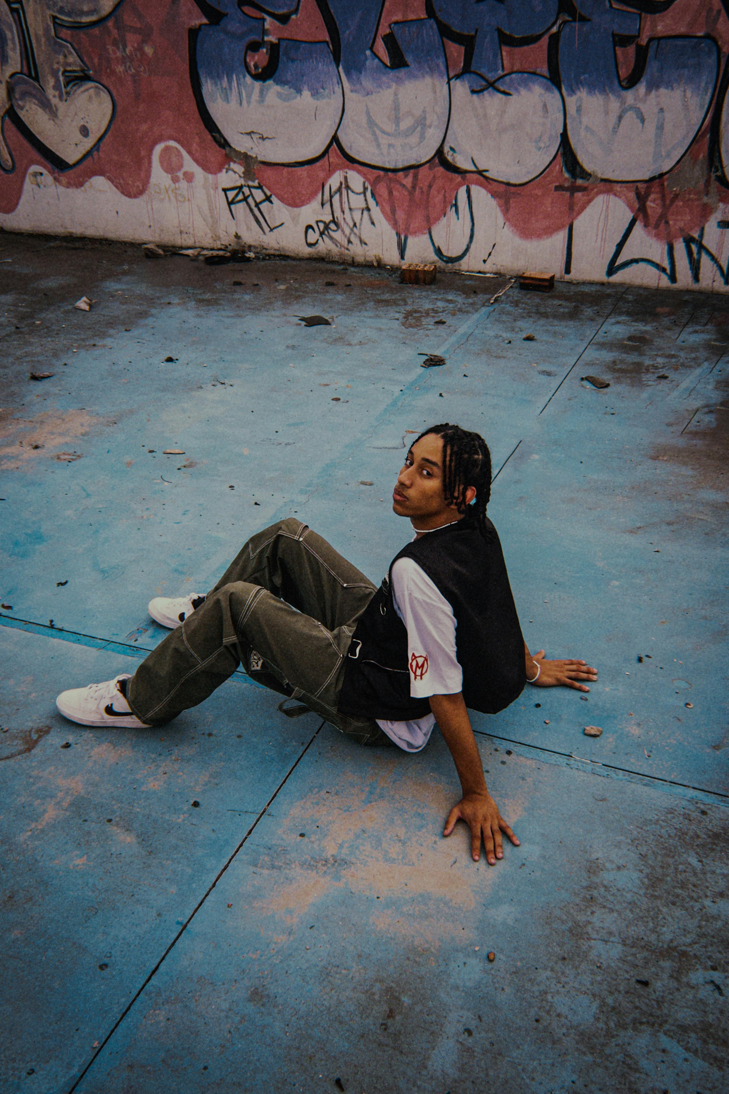 Young adult sitting on a colorful, graffiti-covered surface outdoors.