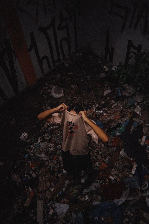 Free Person standing in a littered, graffiti-filled alleyway, showcasing urban decay. Stock Photo