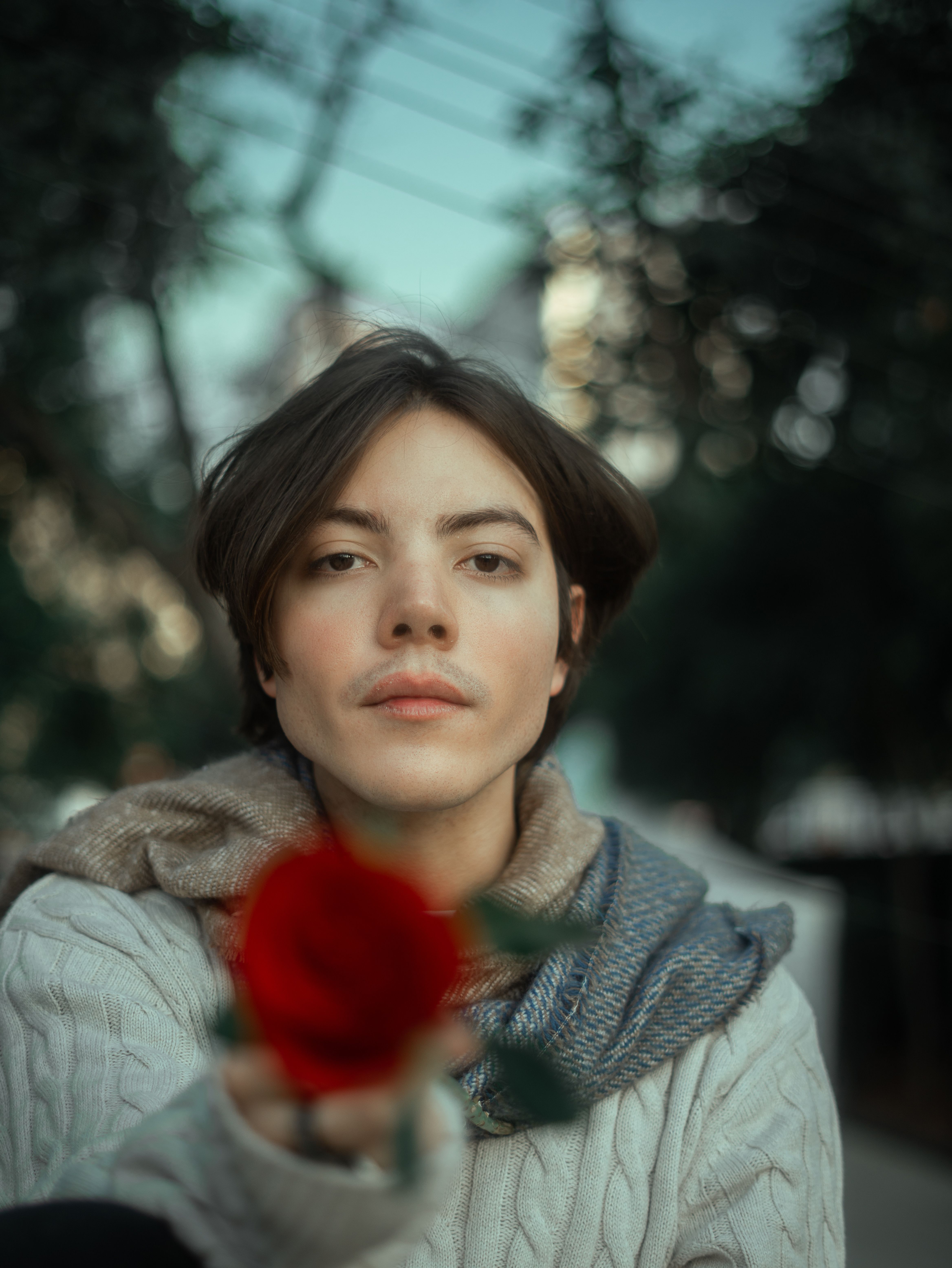 Young adult holding a red rose in a vintage-inspired outdoor setting.