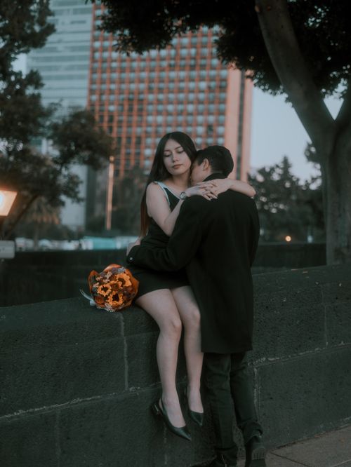 Free A romantic couple embraces on a city wall in Mexico City, featuring a warm, cinematic atmosphere. Stock Photo
