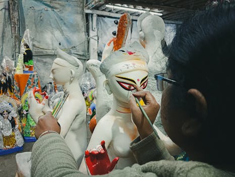An artist skillfully paints a traditional Hindu idol in a workshop filled with vibrant cultural artworks.