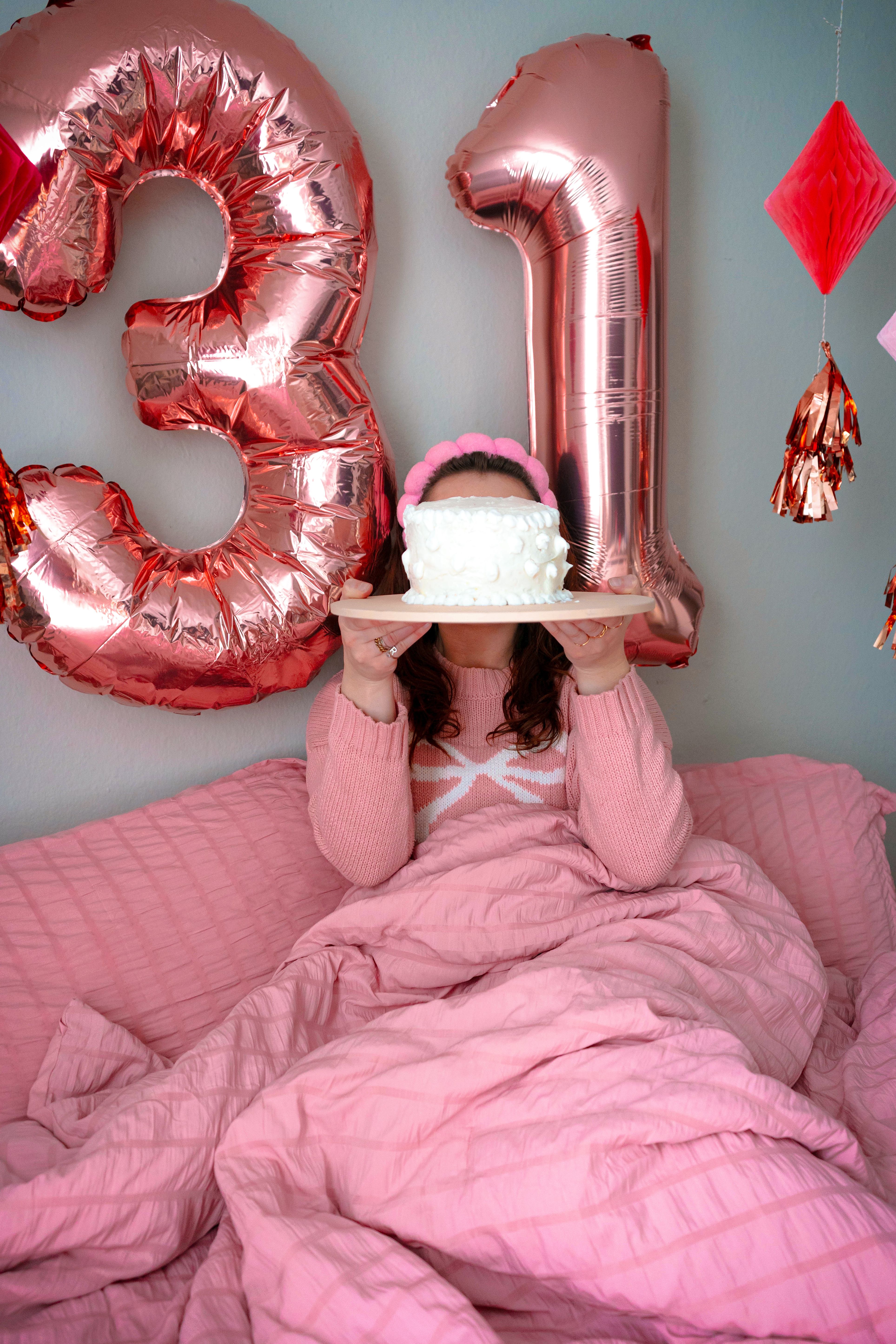 A woman celebrates her 31st birthday with pink decor and a cake in an indoor setting.