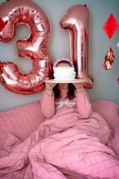 A woman celebrates her 31st birthday with pink decor and a cake in an indoor setting.