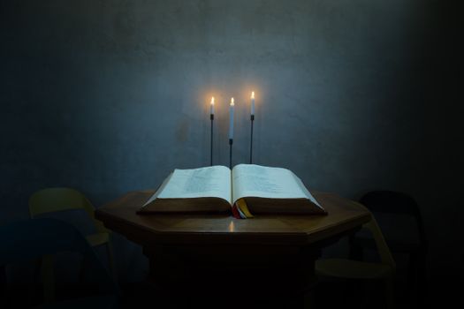 An open book on a wooden table illuminated by three candles, casting a serene glow.