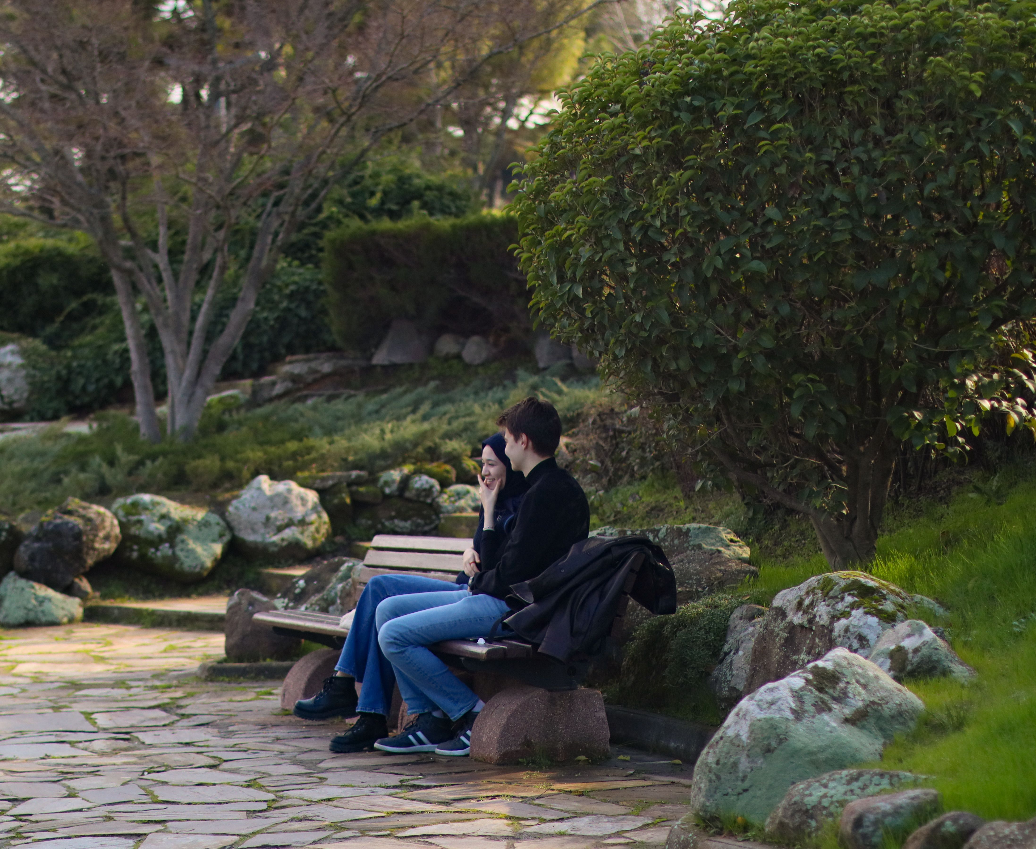 Two people sitting on a park bench surrounded by lush greenery, enjoying a quiet moment.