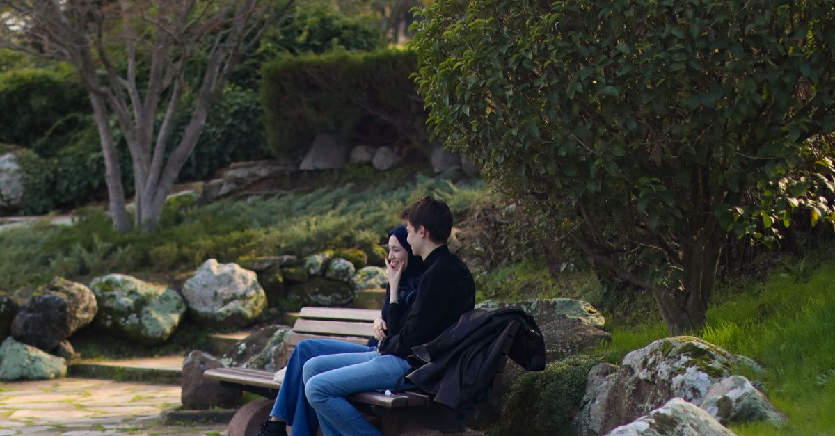 Two people sitting on a park bench surrounded by lush greenery, enjoying a quiet moment.