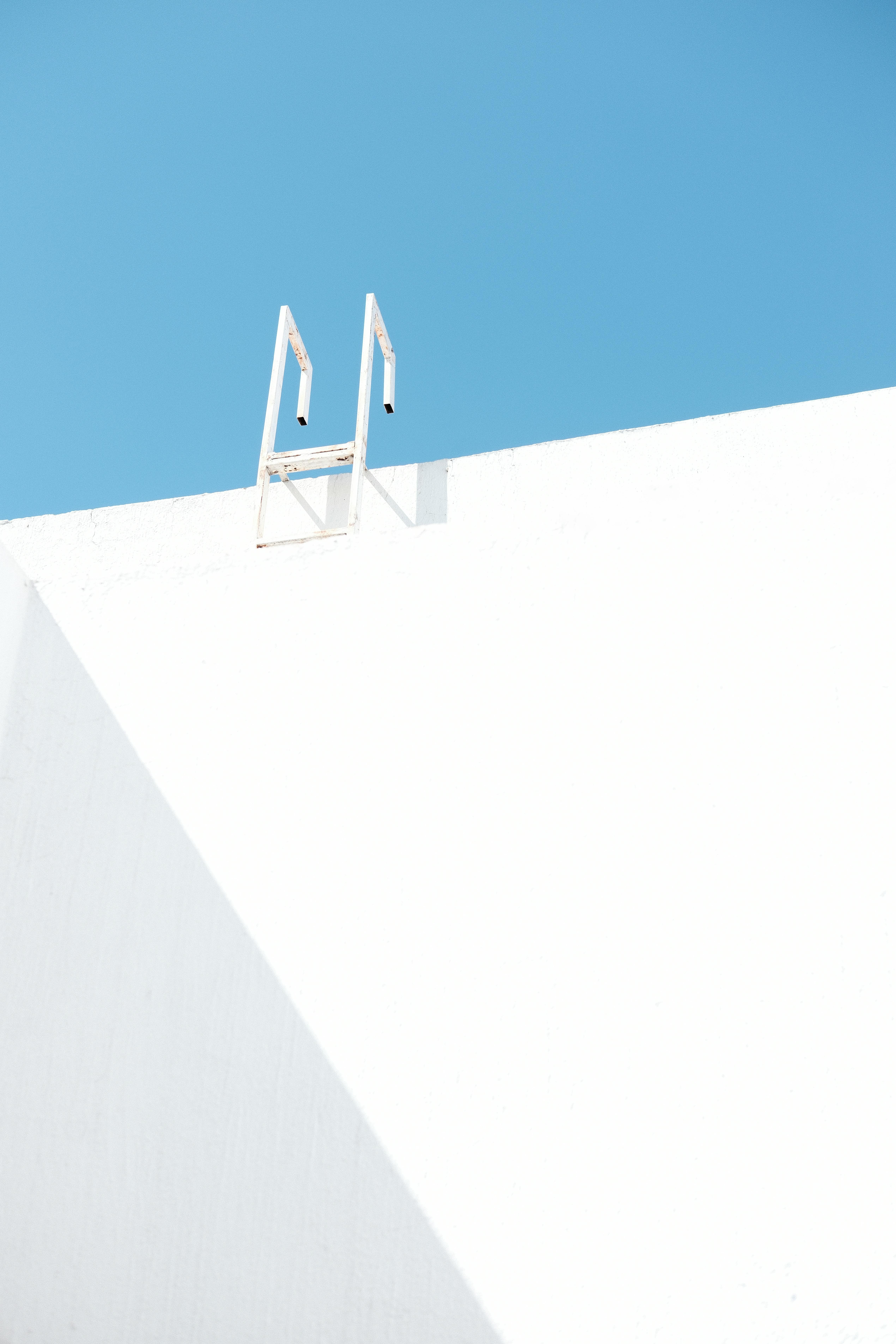 Abstract minimalist photograph of a white wall with a ladder against a bright blue sky.