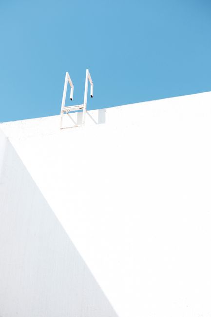 Abstract minimalist photograph of a white wall with a ladder against a bright blue sky.
