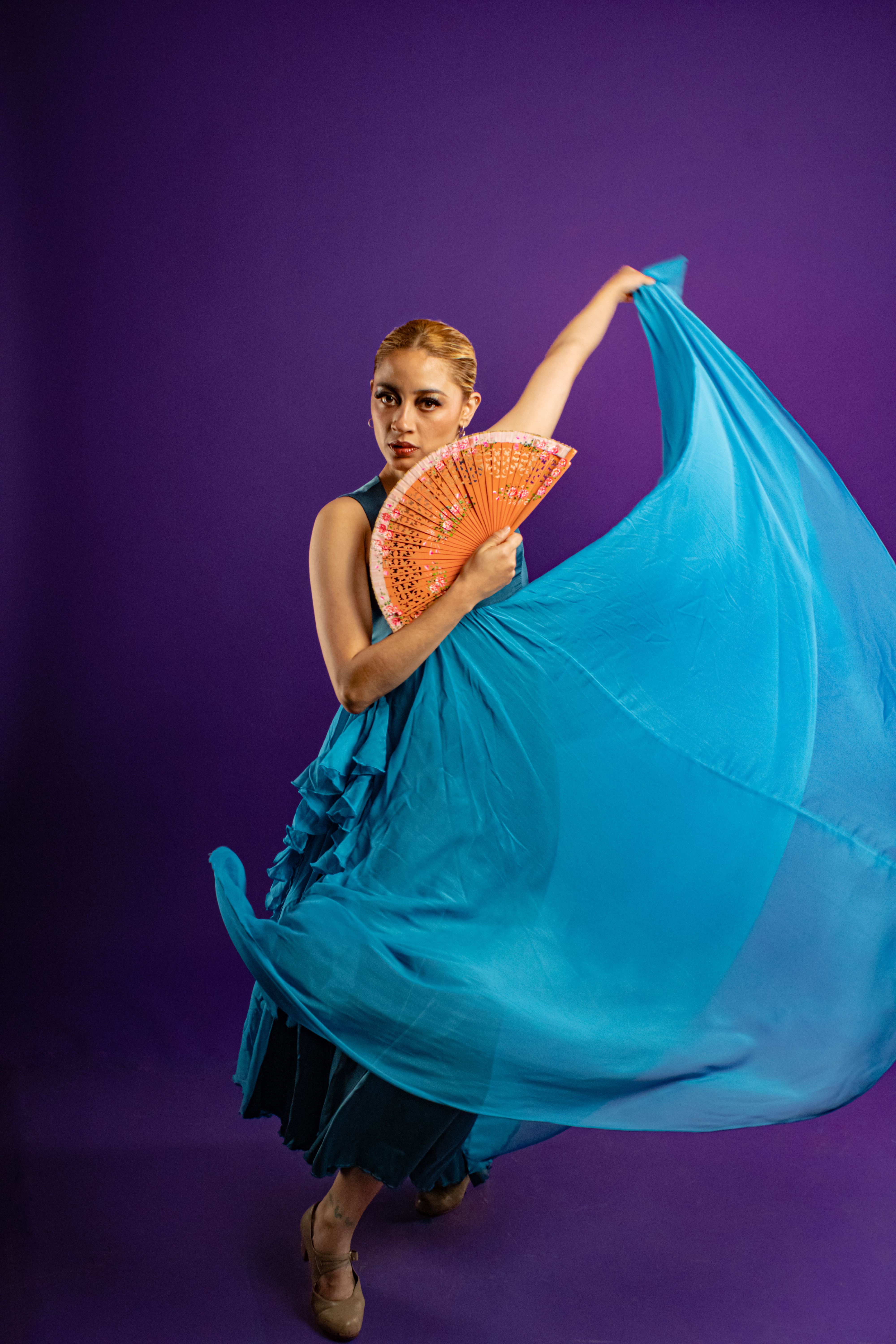 Flamenco dancer in a blue dress with an orange fan on a blue background, showcasing expressive dance.