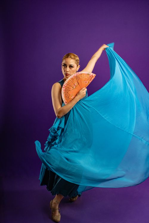 Free Flamenco dancer in a blue dress with an orange fan on a blue background, showcasing expressive dance. Stock Photo