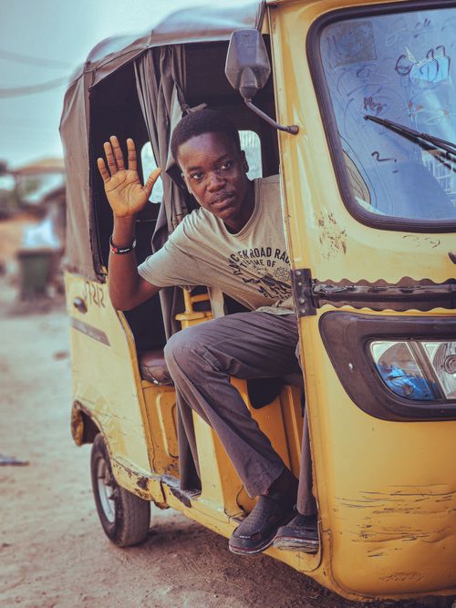 Free A smiling man waves from a yellow auto rickshaw parked outdoors, showcasing urban lifestyle. Stock Photo