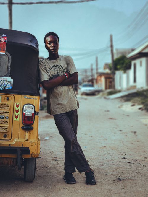 Free A young man casually leans on a yellow auto-rickshaw in a residential urban setting, showcasing local street life. Stock Photo