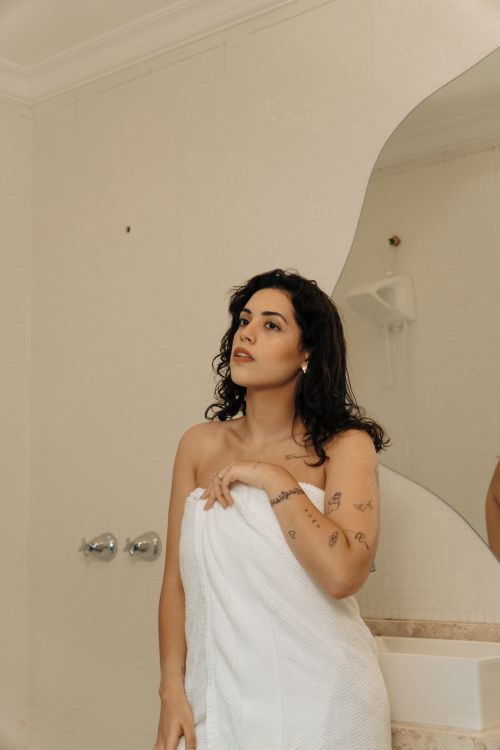 Free Young woman in bathroom with towel, gazing to the side. Minimalist decor. Stock Photo